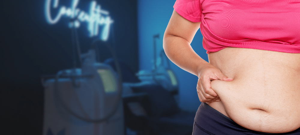 An image of a person holding their stubborn belly fat, standing in front of a CoolSculpting machine.