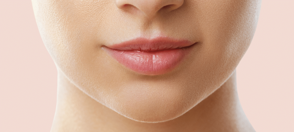 A woman's lower face focused on her lips, with a pink background.